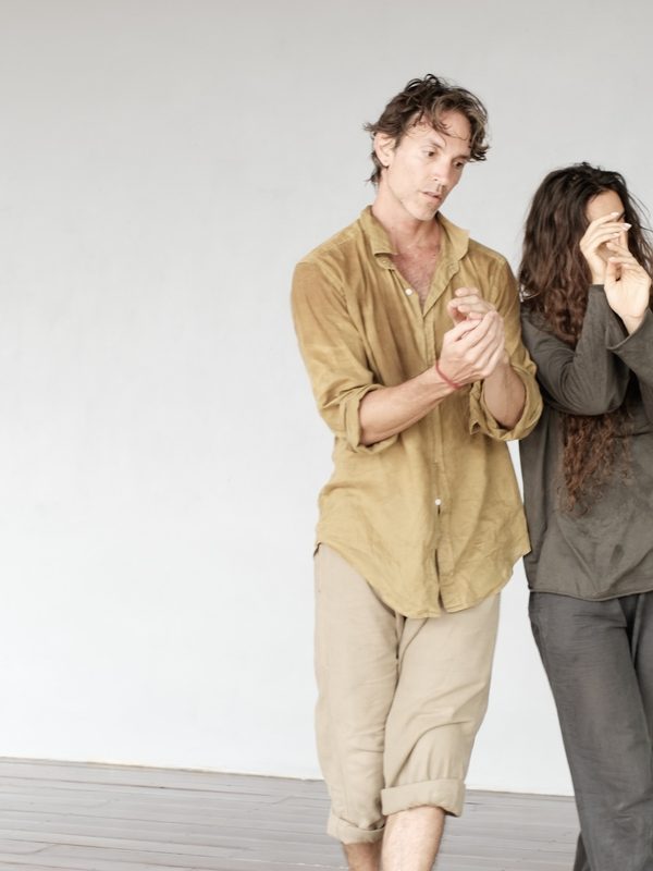 Two dancers walking close together, hands touching.